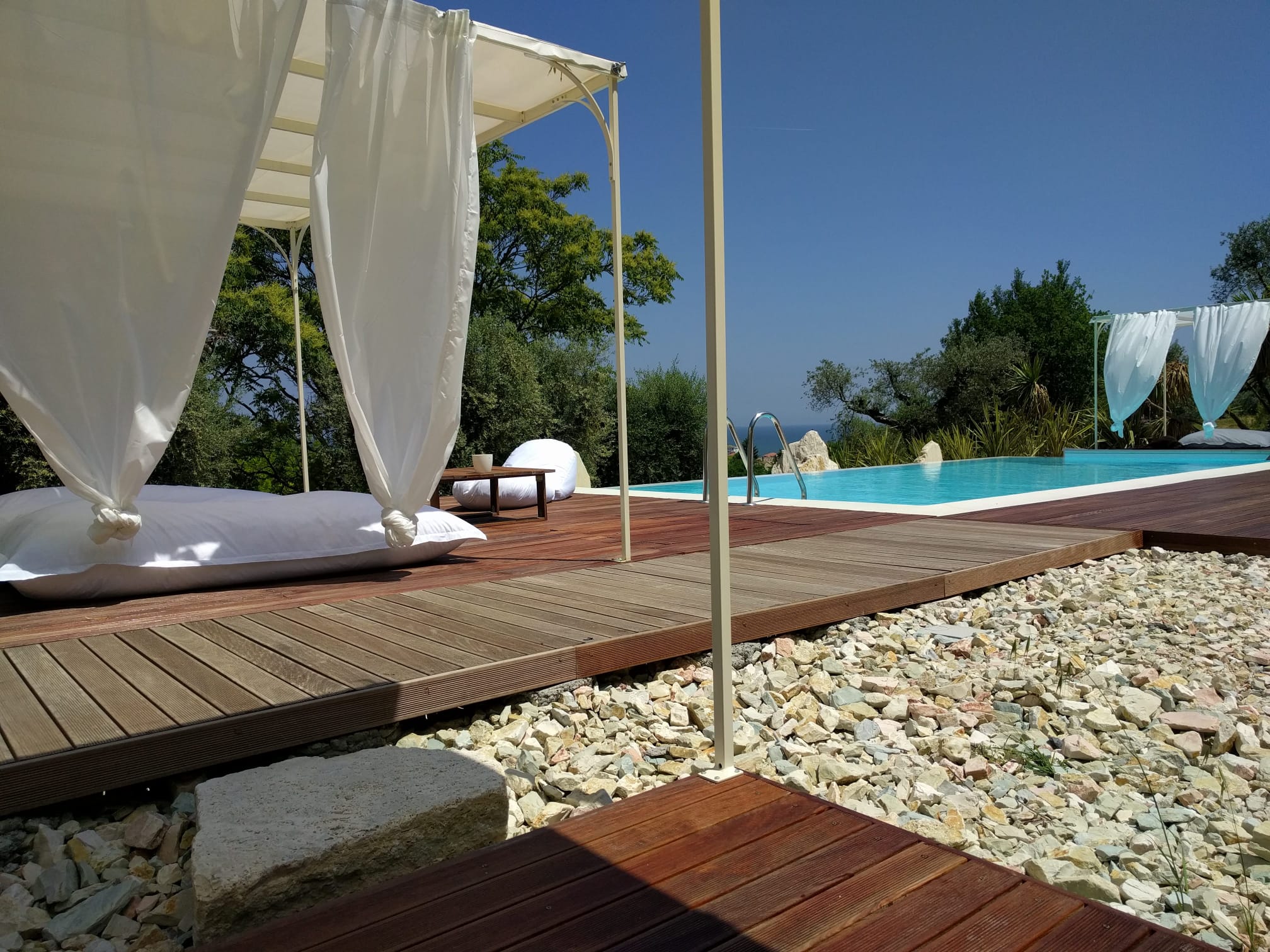 Wooden sun deck with canopy daybeds beside the infinity pool, sea beyond